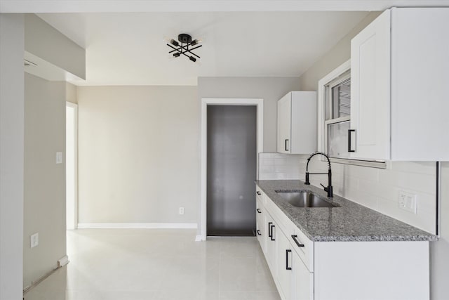 kitchen with white cabinetry, sink, dark stone countertops, decorative backsplash, and light tile patterned floors