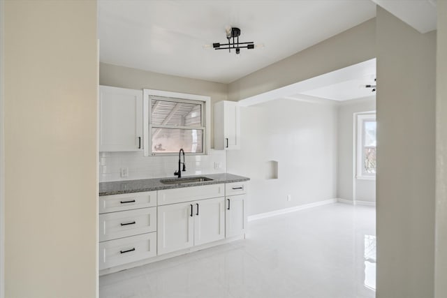 kitchen with stone counters, backsplash, white cabinetry, and sink