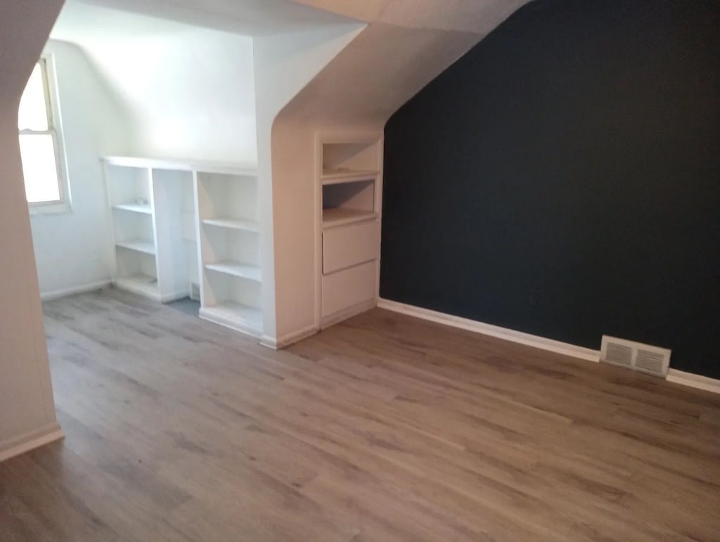 bonus room featuring wood-type flooring, vaulted ceiling, and built in features