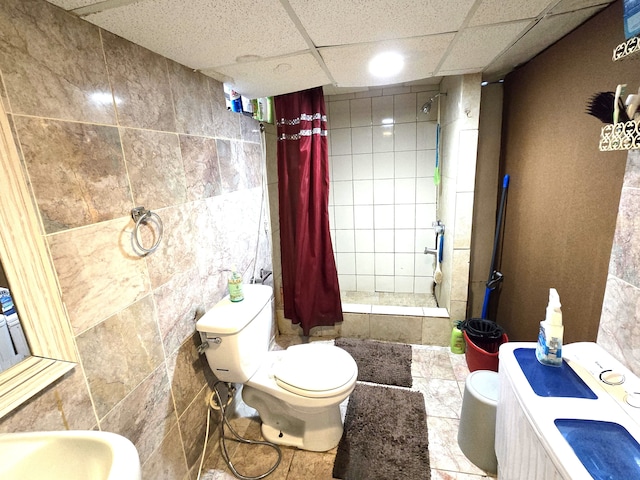 bathroom with a drop ceiling, toilet, walk in shower, and tile walls