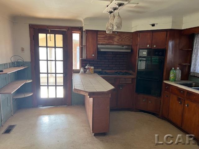 kitchen featuring under cabinet range hood, visible vents, tile counters, decorative backsplash, and black appliances