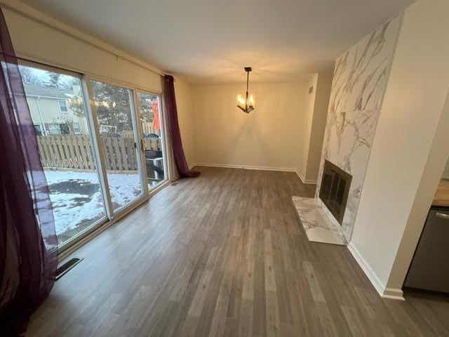 unfurnished living room featuring dark hardwood / wood-style flooring, a stone fireplace, and an inviting chandelier