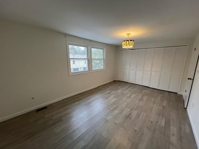 unfurnished bedroom featuring hardwood / wood-style floors, a notable chandelier, and a closet