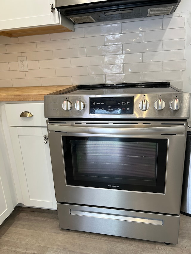 interior details featuring electric stove, tasteful backsplash, and white cabinets