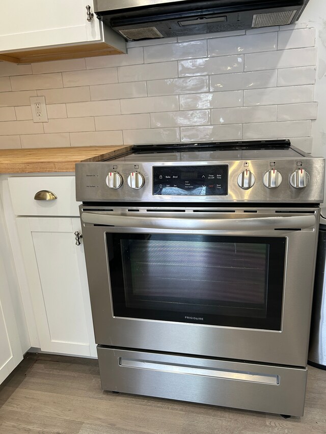 1622 Brentwood Dr, Troy, MI 48098 - kitchen view of stainless steel range with electric stovetop, white cabinetry, wood finished floors, tasteful backsplash, and extractor fan