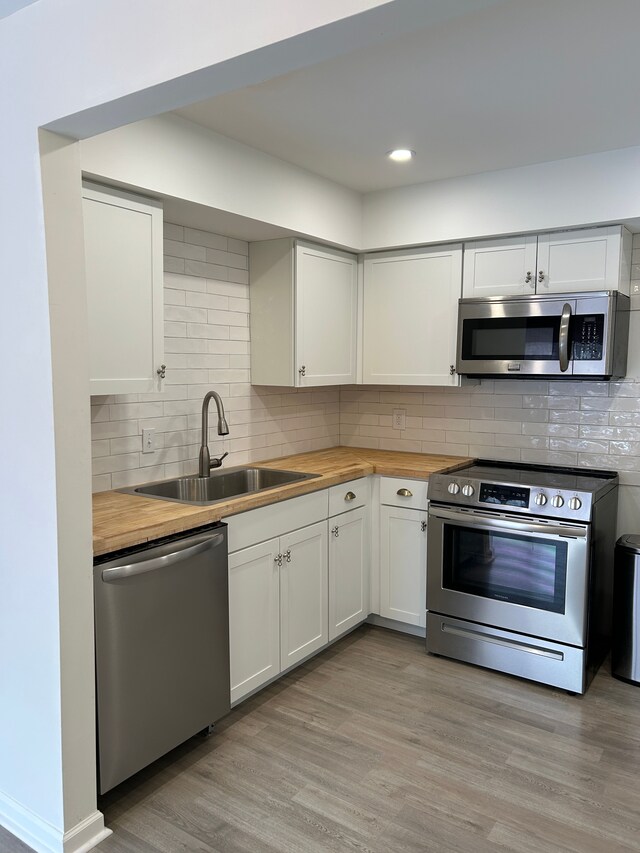 1622 Brentwood Dr, Troy, MI 48098 - kitchen with appliances with stainless steel finishes, butcher block countertops, a sink, light wood finished floors, and decorative backsplash