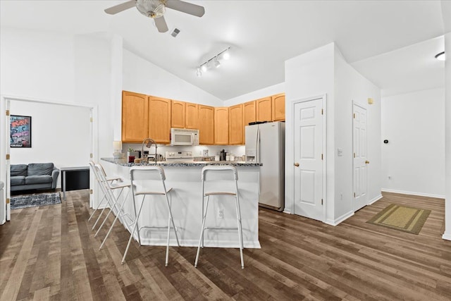 kitchen featuring a breakfast bar, white appliances, dark hardwood / wood-style floors, stone countertops, and kitchen peninsula