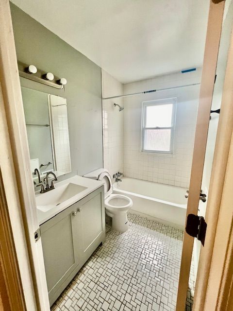 full bathroom featuring vanity, tiled shower / bath combo, and toilet