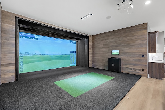 playroom featuring light hardwood / wood-style floors, golf simulator, wooden walls, and sink