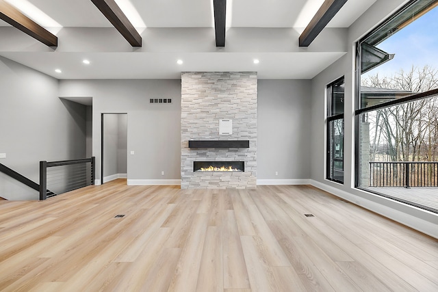 unfurnished living room featuring beamed ceiling, a healthy amount of sunlight, light wood-type flooring, and a fireplace