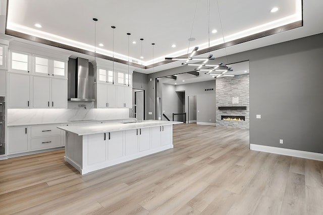 kitchen featuring decorative light fixtures, white cabinetry, a large island, and wall chimney range hood