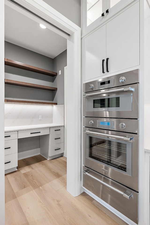 kitchen with tasteful backsplash, light hardwood / wood-style floors, white cabinetry, and double oven