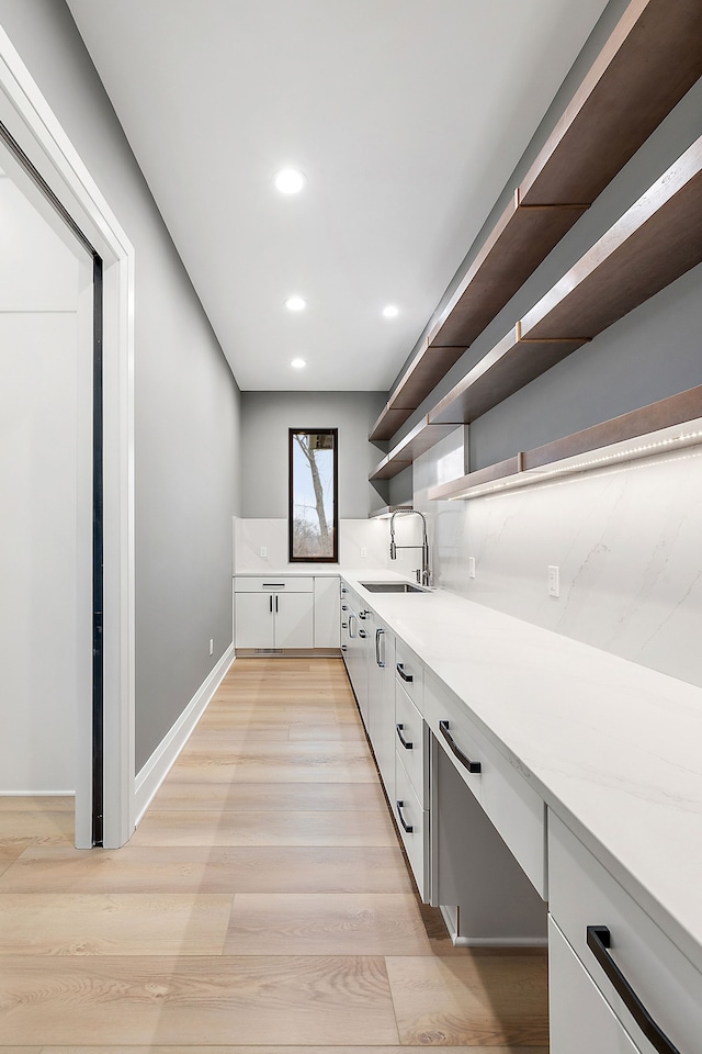 interior space with decorative backsplash, light wood-type flooring, sink, built in desk, and white cabinetry