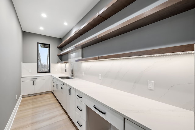 kitchen with white cabinets, backsplash, light hardwood / wood-style flooring, and sink