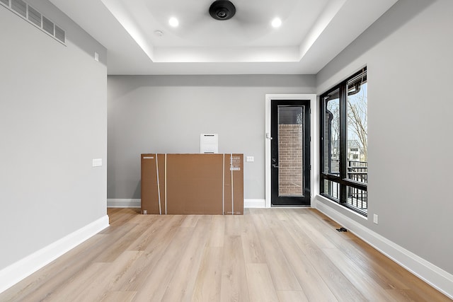 spare room with a tray ceiling and light wood-type flooring