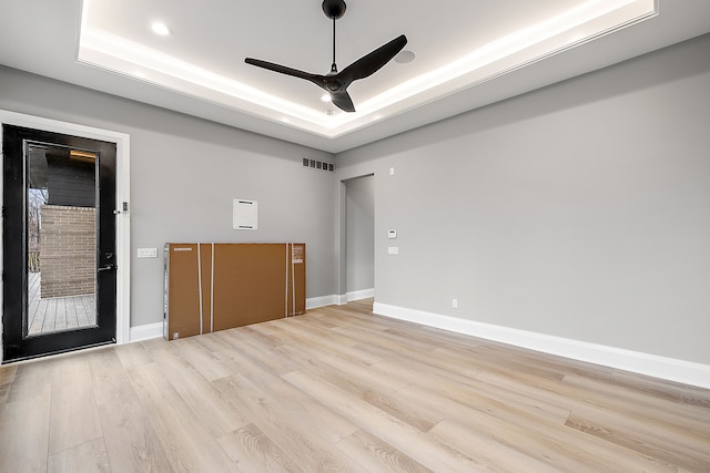 empty room with a tray ceiling, ceiling fan, and light hardwood / wood-style floors