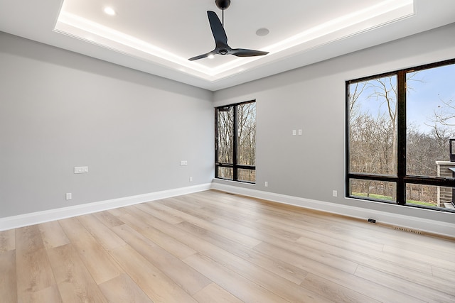 unfurnished room featuring ceiling fan, light hardwood / wood-style flooring, and a tray ceiling