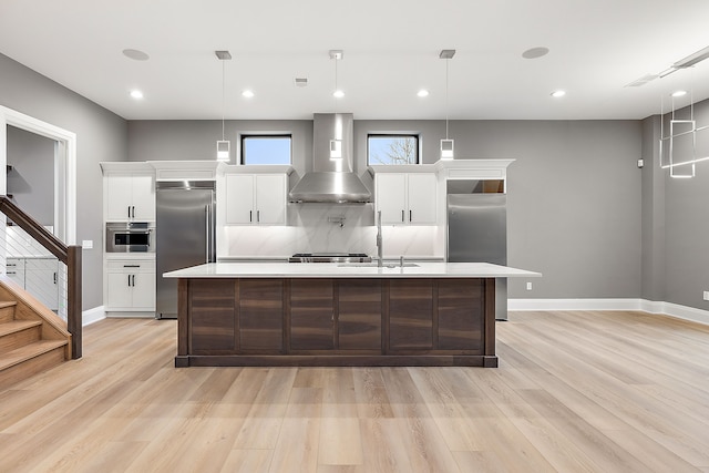 kitchen with white cabinets, wall chimney exhaust hood, stainless steel built in refrigerator, and hanging light fixtures