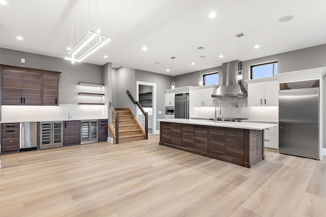 kitchen with stainless steel fridge, high quality fridge, dark brown cabinetry, wall chimney range hood, and pendant lighting