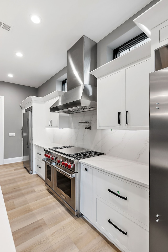 kitchen featuring white cabinetry, high quality appliances, tasteful backsplash, and wall chimney exhaust hood