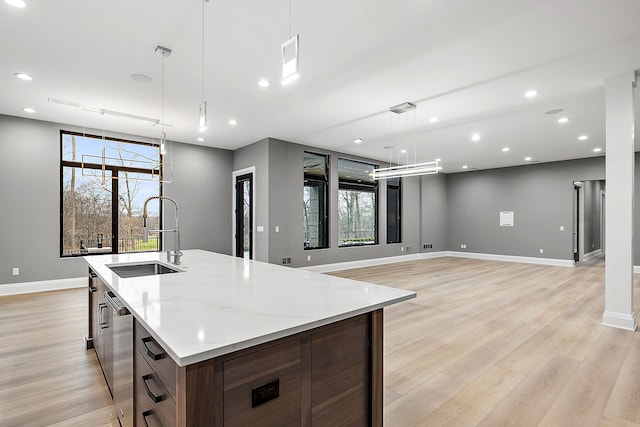 kitchen featuring light stone countertops, light wood-type flooring, sink, pendant lighting, and a large island with sink