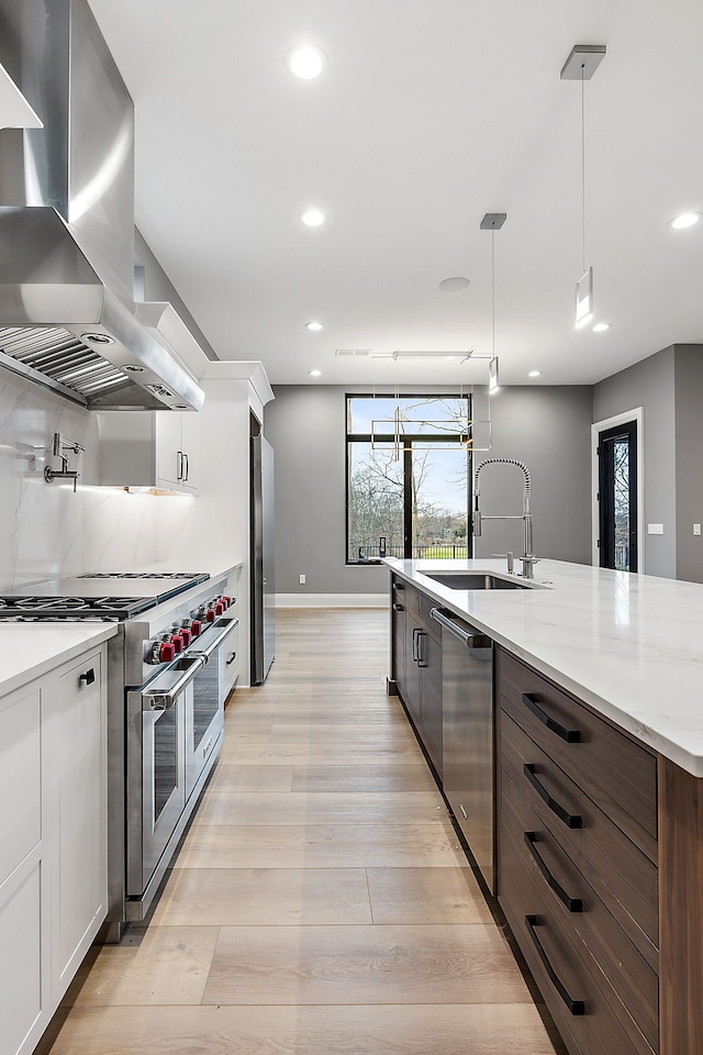 kitchen featuring pendant lighting, white cabinets, wall chimney range hood, sink, and stainless steel appliances