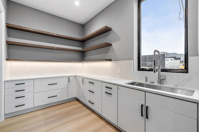 kitchen with white cabinets, light wood-type flooring, tasteful backsplash, and sink