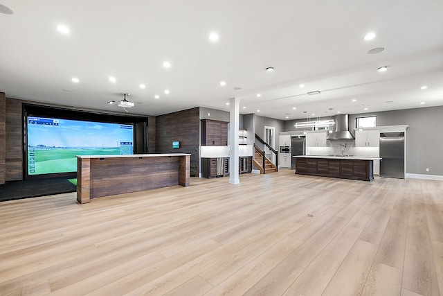 kitchen featuring a center island with sink, wall chimney exhaust hood, light hardwood / wood-style floors, and dark brown cabinets