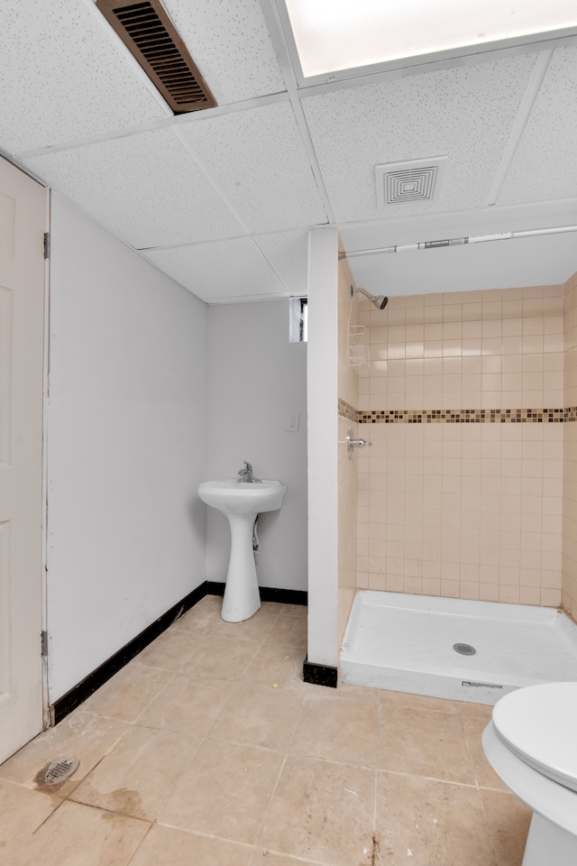 bathroom featuring a tile shower, tile patterned flooring, toilet, and a drop ceiling