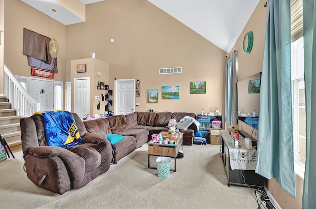 carpeted living room with visible vents, stairs, and high vaulted ceiling