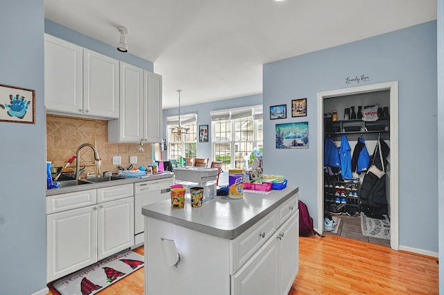 kitchen featuring decorative backsplash, white dishwasher, a center island, white cabinets, and light wood-style floors