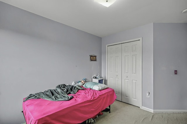 bedroom with baseboards, a closet, and light colored carpet