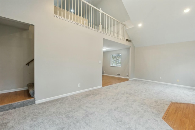 unfurnished living room with visible vents, baseboards, light colored carpet, stairs, and high vaulted ceiling