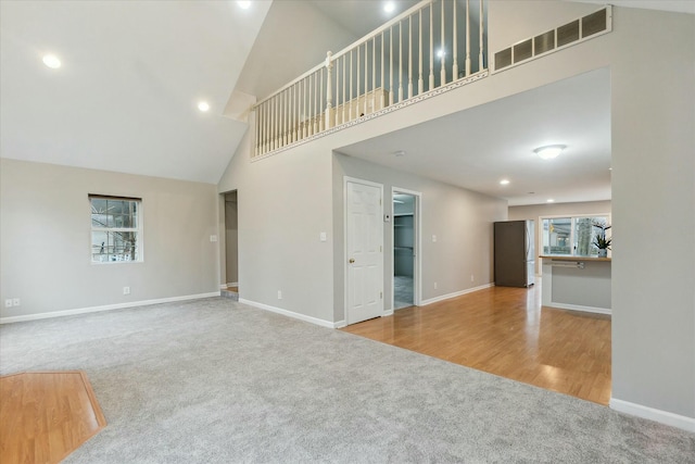 unfurnished living room featuring light colored carpet, visible vents, a towering ceiling, and baseboards