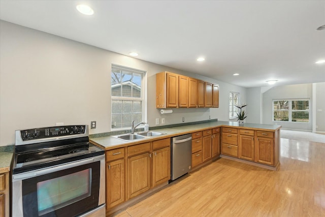 kitchen with light wood-style flooring, stainless steel appliances, a peninsula, a sink, and light countertops