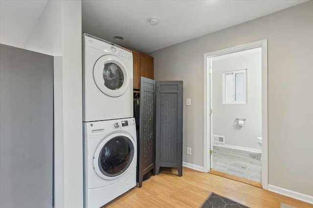 laundry room featuring laundry area, visible vents, baseboards, light wood-style floors, and stacked washing maching and dryer