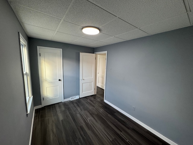 unfurnished bedroom with a drop ceiling and dark wood-type flooring