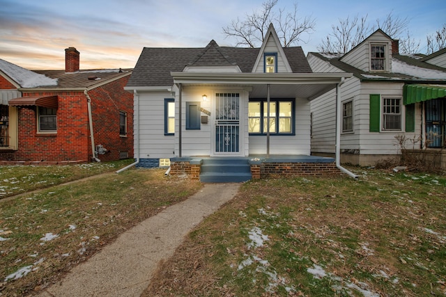 view of front of home with covered porch, roof with shingles, and a lawn