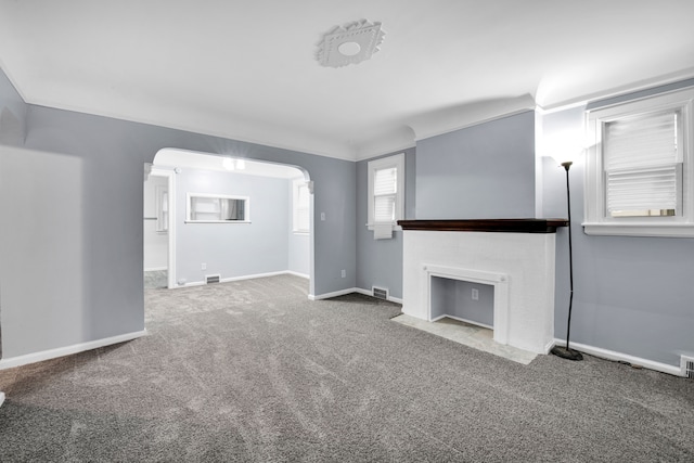 unfurnished living room featuring baseboards, arched walkways, a fireplace with flush hearth, ornamental molding, and carpet flooring