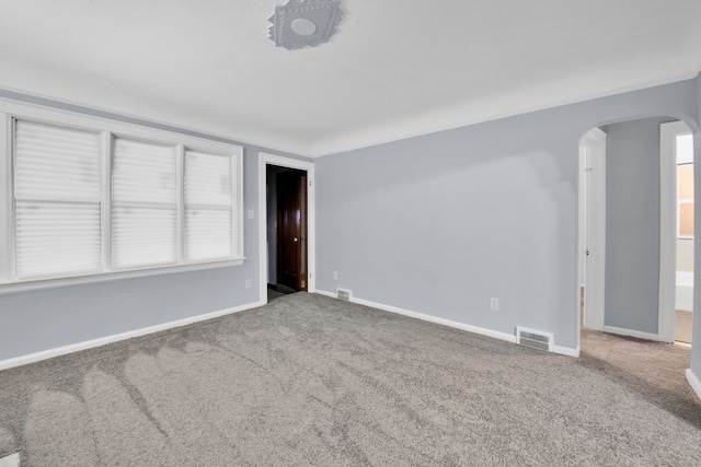 carpeted spare room with arched walkways, visible vents, and baseboards