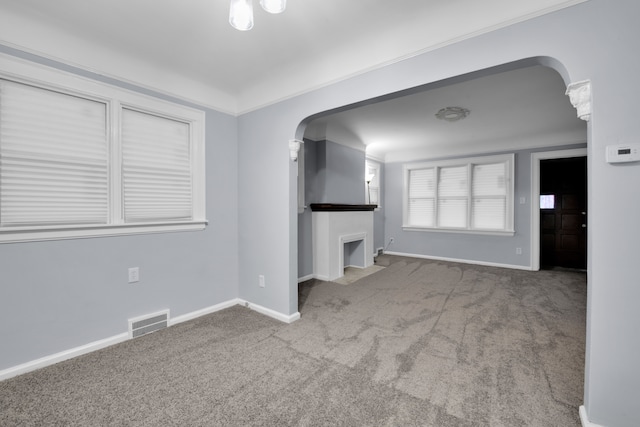 unfurnished living room with arched walkways, carpet floors, visible vents, and baseboards