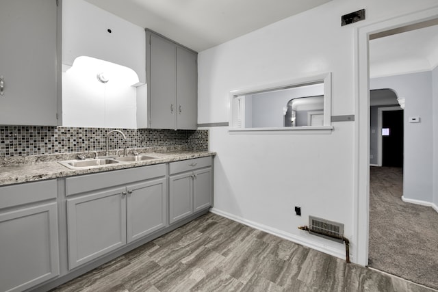 kitchen with arched walkways, gray cabinetry, a sink, visible vents, and backsplash