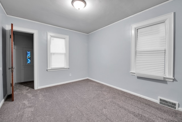 carpeted spare room featuring baseboards, visible vents, and crown molding