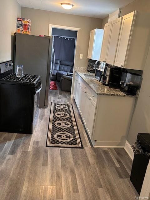 kitchen featuring stainless steel refrigerator, white cabinetry, light stone counters, and black range with electric cooktop