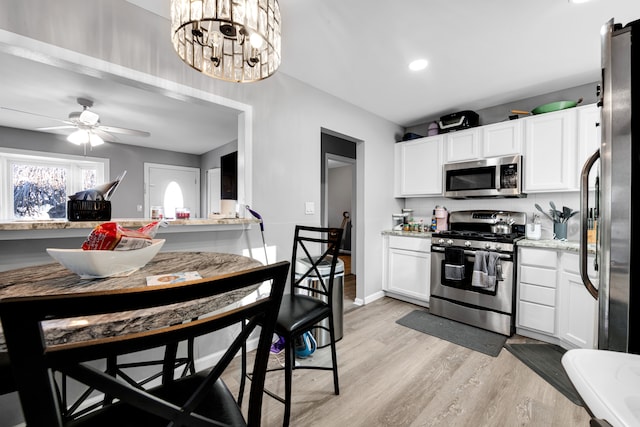 kitchen with white cabinetry, stainless steel appliances, light stone counters, light hardwood / wood-style flooring, and ceiling fan with notable chandelier