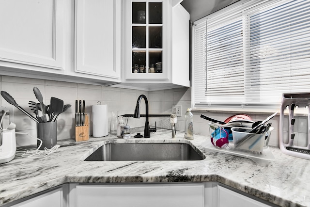 kitchen featuring decorative backsplash, light stone counters, sink, and white cabinets