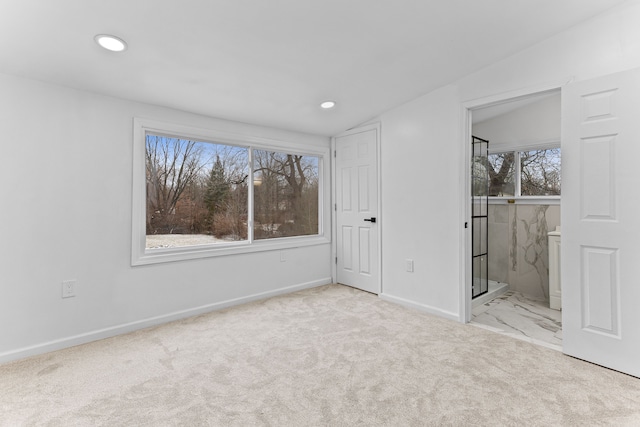 unfurnished bedroom featuring ensuite bath, light carpet, and vaulted ceiling