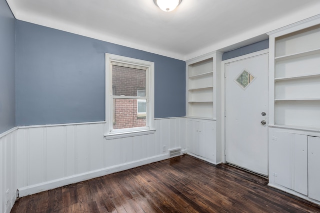 spare room featuring built in shelves and dark hardwood / wood-style floors