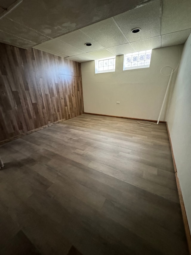 basement featuring wood walls, a drop ceiling, and wood-type flooring