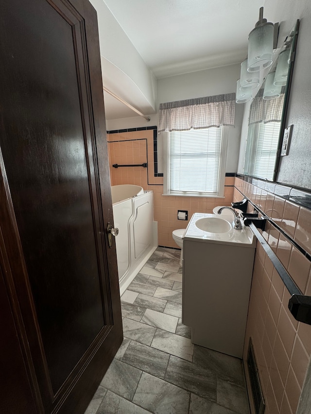 bathroom featuring vanity, toilet, tile walls, and a bathing tub